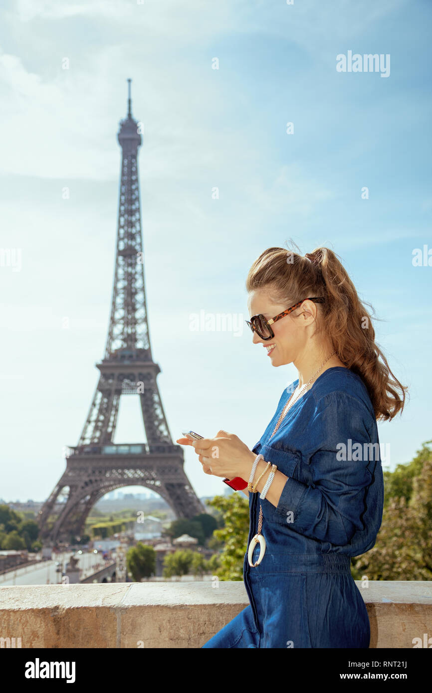 happy stylish woman in blue jeans overall in the front of Eiffel tower in  Paris, France watching video in internet via mobile phone Stock Photo -  Alamy