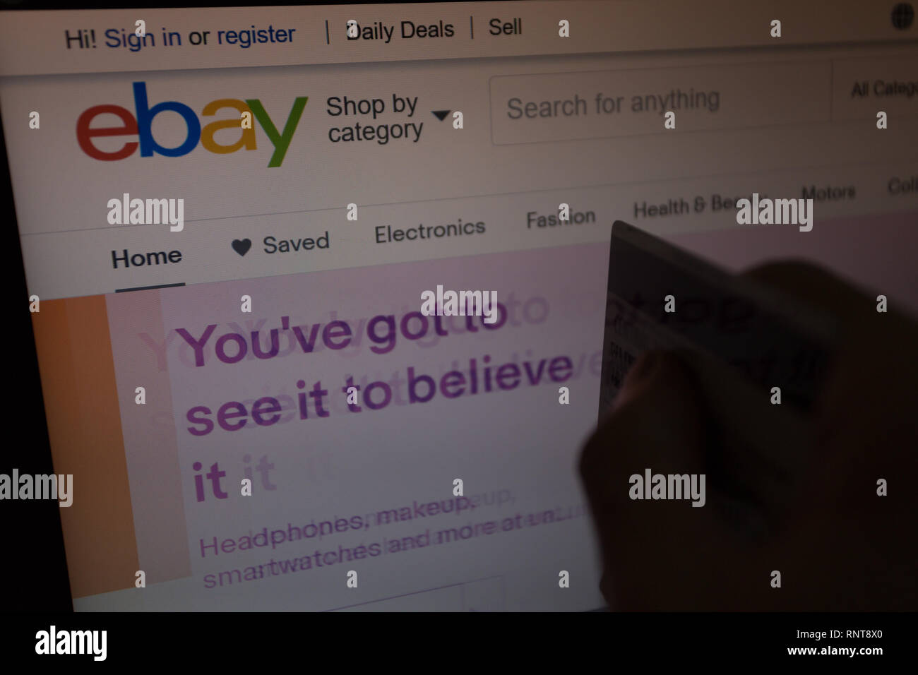 eBay logo on its website is shown on laptop computer screen, hand holding credit debit card unfocused on foreground, online shoppers, purchases Stock Photo