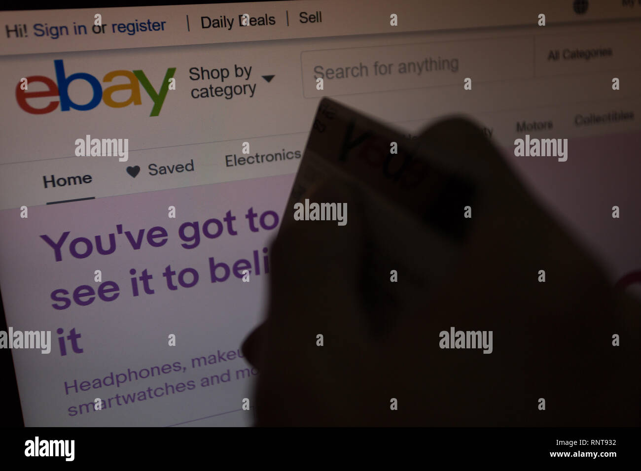 eBay logo on its website is shown on laptop computer screen, hand holding credit debit card unfocused on foreground, online shoppers, purchases Stock Photo