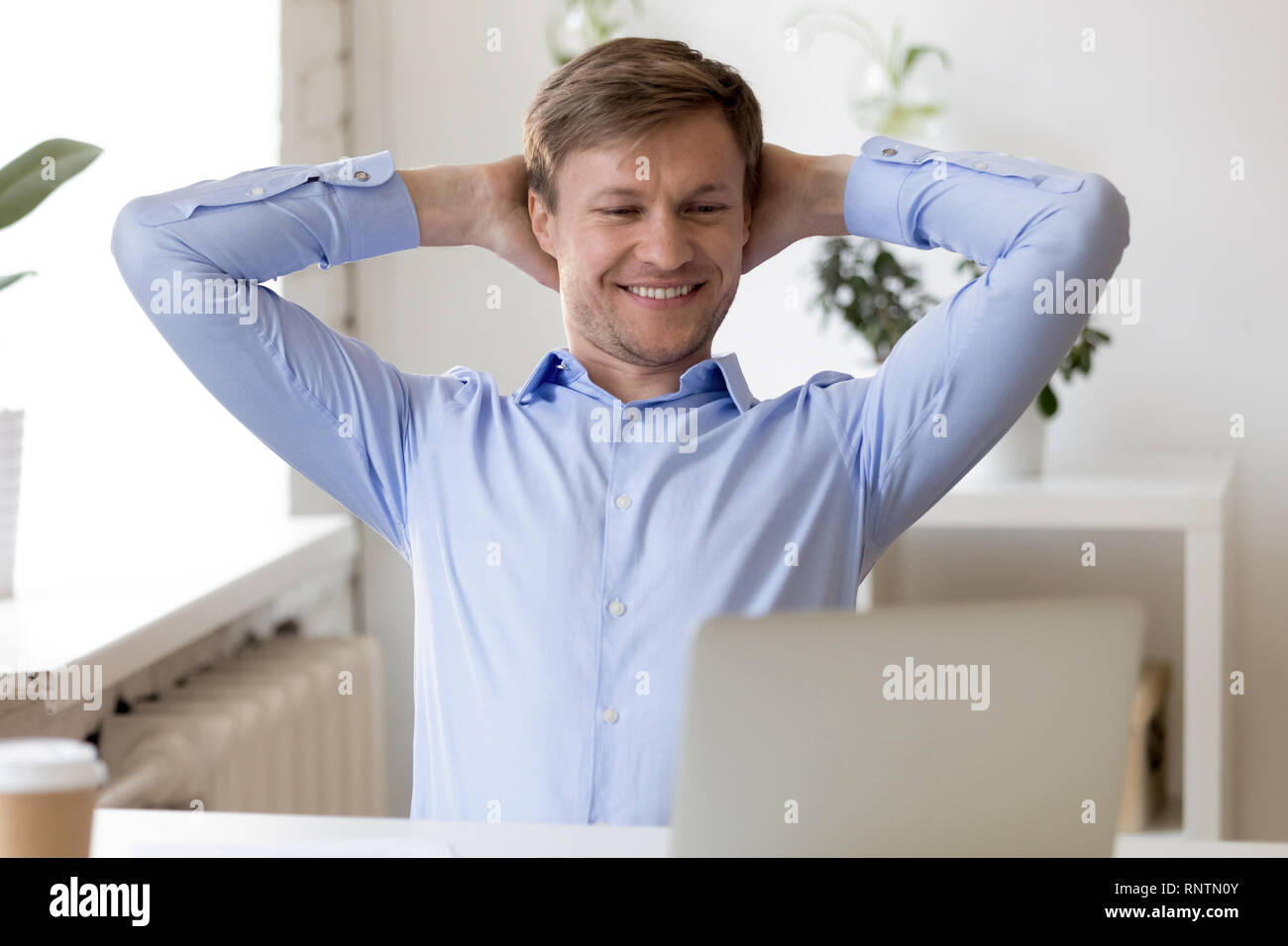 Satisfied businessman sitting at desk put hands behind head Stock Photo