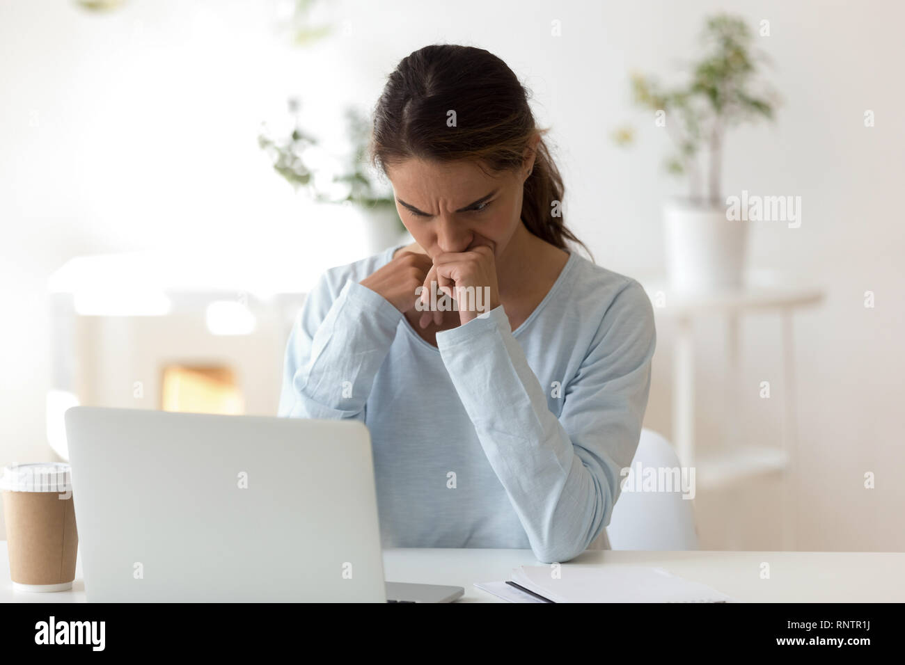 Gloomy young woman sitting at desk looking at computer screen Stock Photo