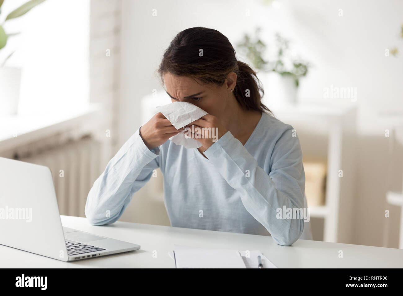Unhealthy female sitting at workplace blowing nose Stock Photo