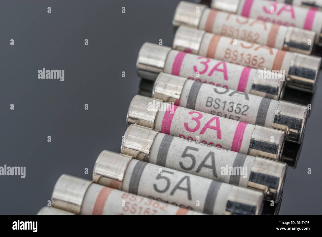 Domestic appliance 3A, 5A & 13A electrical fuses (Ceramic Cartridge type) on reflective black background. Metaphor electrical safety. 25mm L x 6.3mm D Stock Photo
