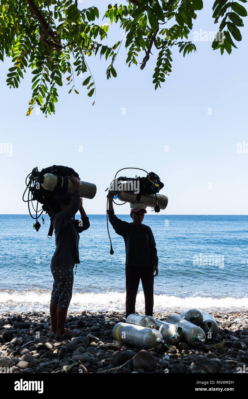 Two women carry heavy scuba diving gear on their heads, a common site