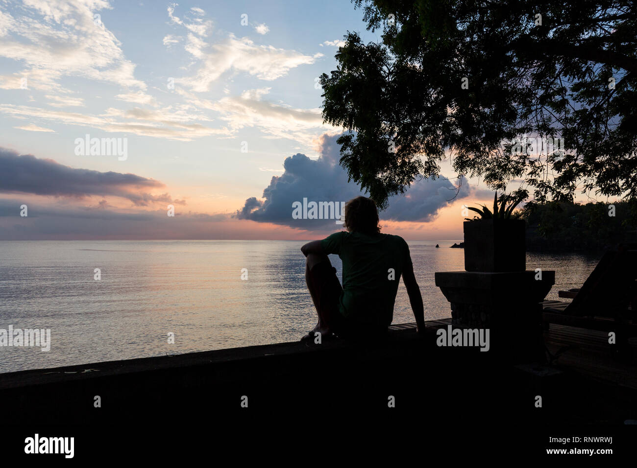 A man looks out at a colorful sunset over the ocean in Tulamben, Bali. Stock Photo