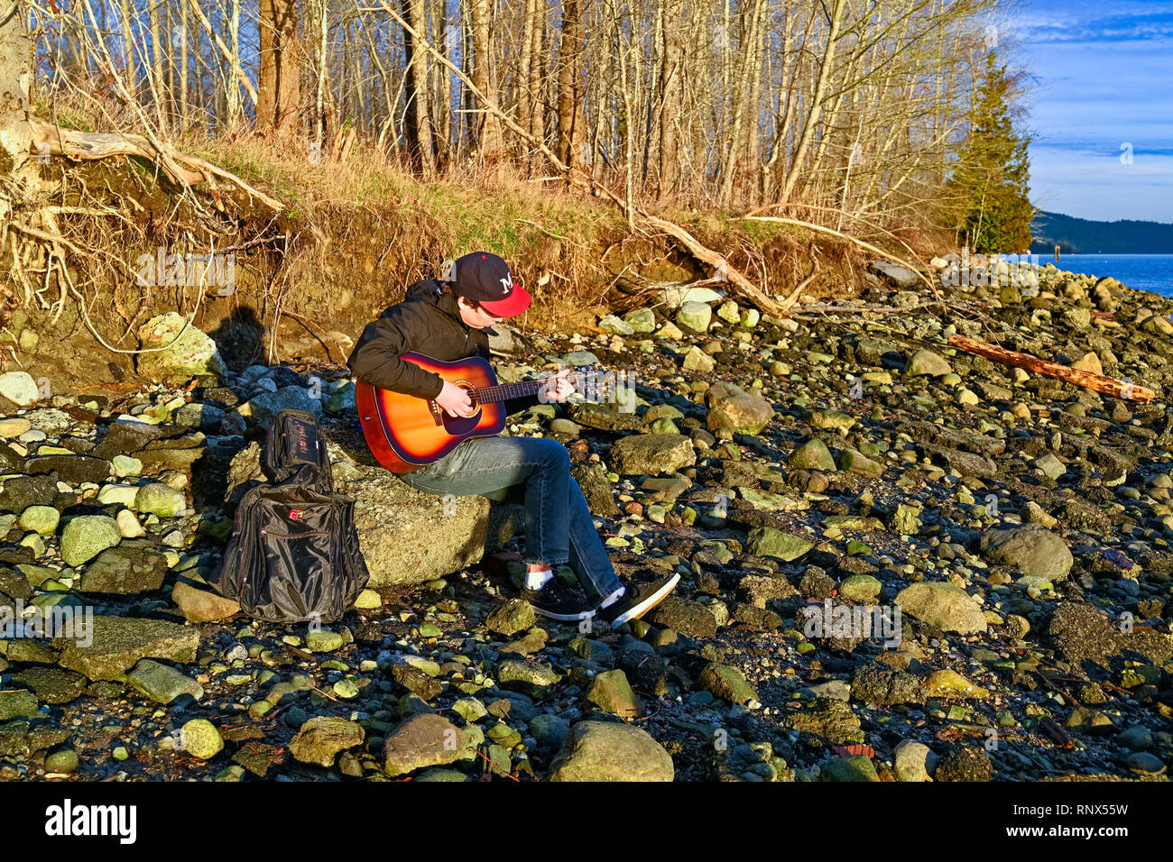 Young man playing guitar on rocky beach Stock Photo