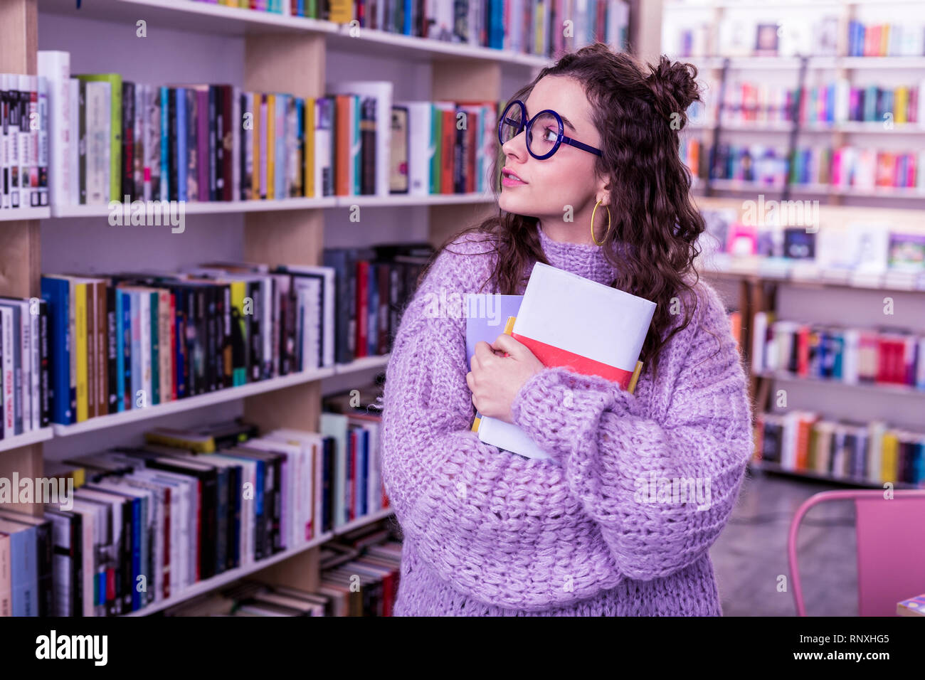 Long-haired appealing girl in oversize sweater carrying bunch of books Stock Photo