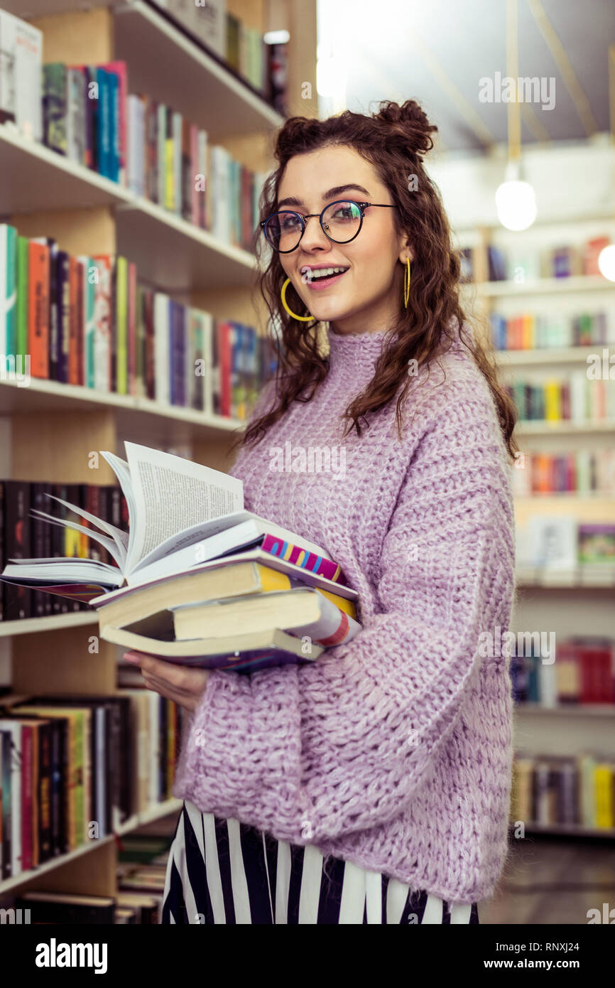 Smiling positive lady holding stack of books while traveling through library Stock Photo