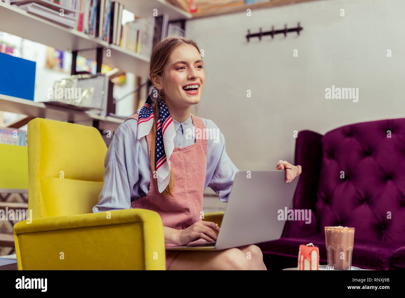 Laughing long-haired lady in pink sleeveless dress closing her laptop Stock Photo