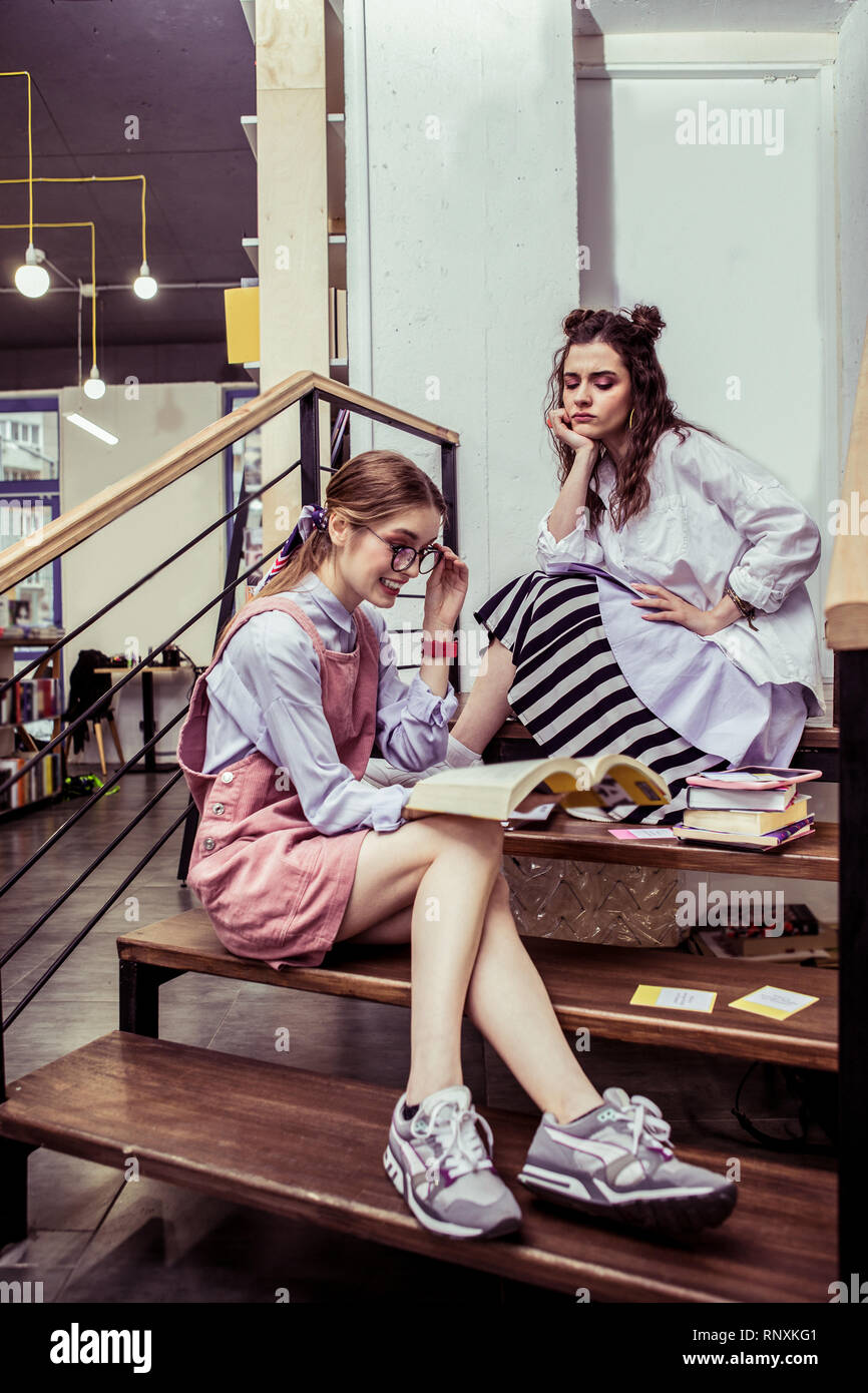 Busy good-looking girls spending time on wooden stairs in co-working area Stock Photo