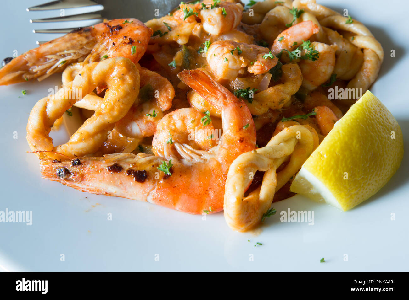 A pasta bowl of Sardinian specialty Lorighittas pasta with seafood and tomato sauce served with fresh lemon wedge garnish. Stock Photo