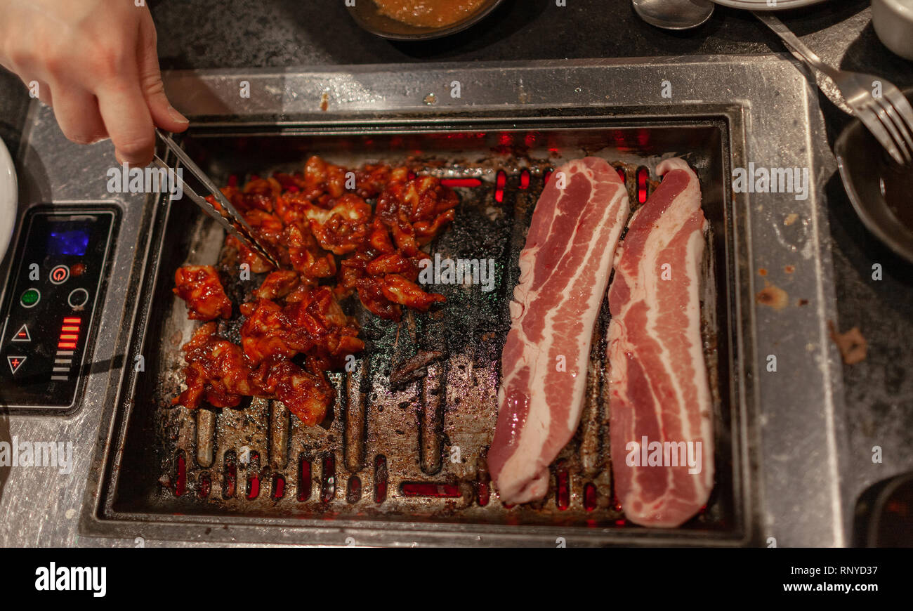 Korean style barbecue with raw pork belly and spicy bulgogi meat on hot stove plate grill Stock