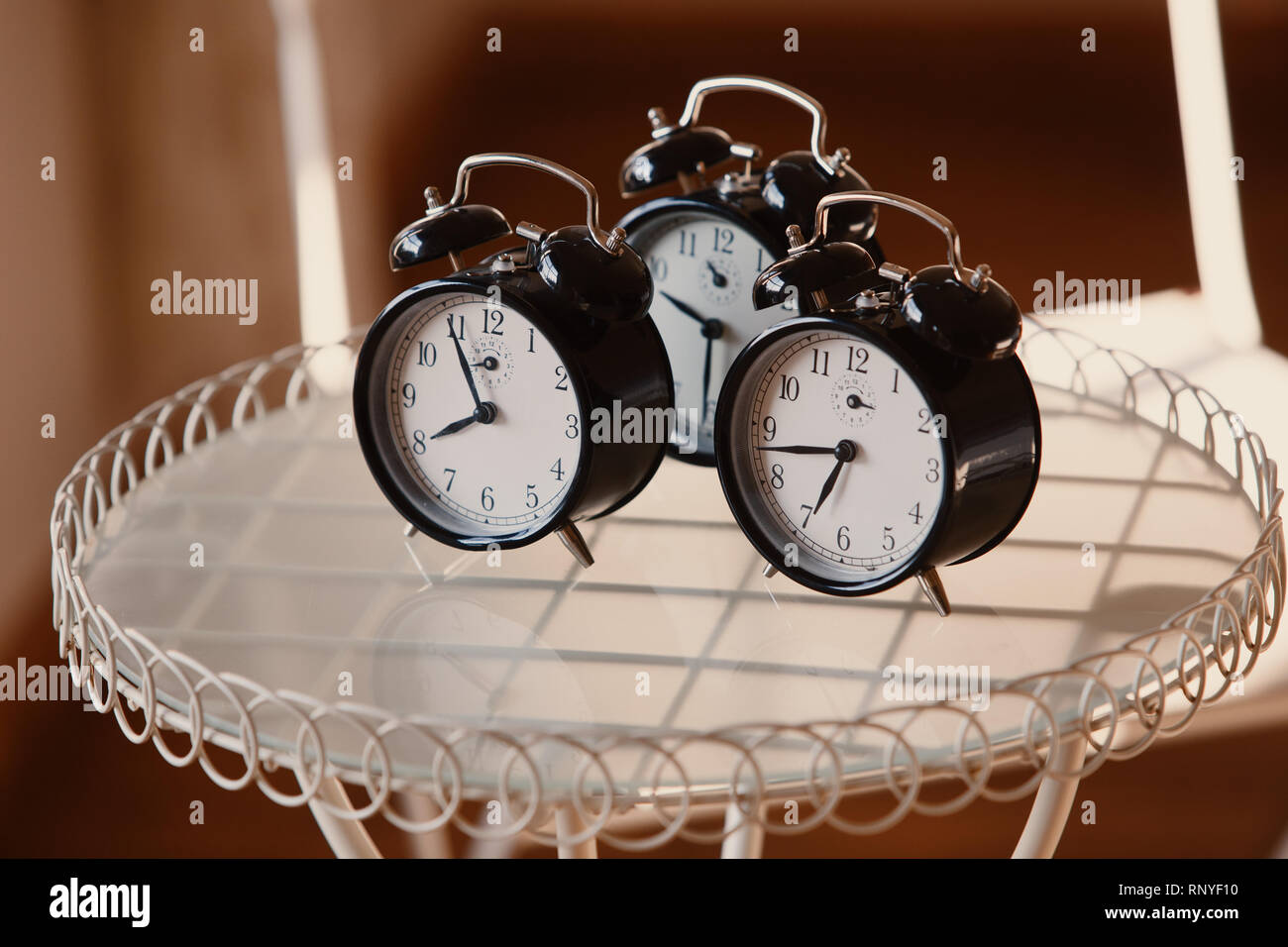 Three alarm clocks on glass table Stock Photo