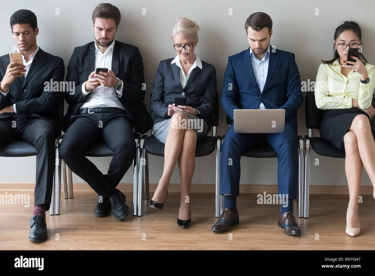 Diverse businesspeople sitting in row using devices phones and laptop Stock Photo