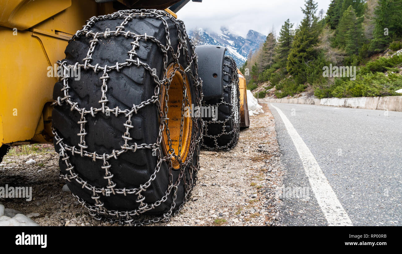 Front loader for snow removal with metal snow chains on wheels. Snow removal in the mountains. Stock Photo
