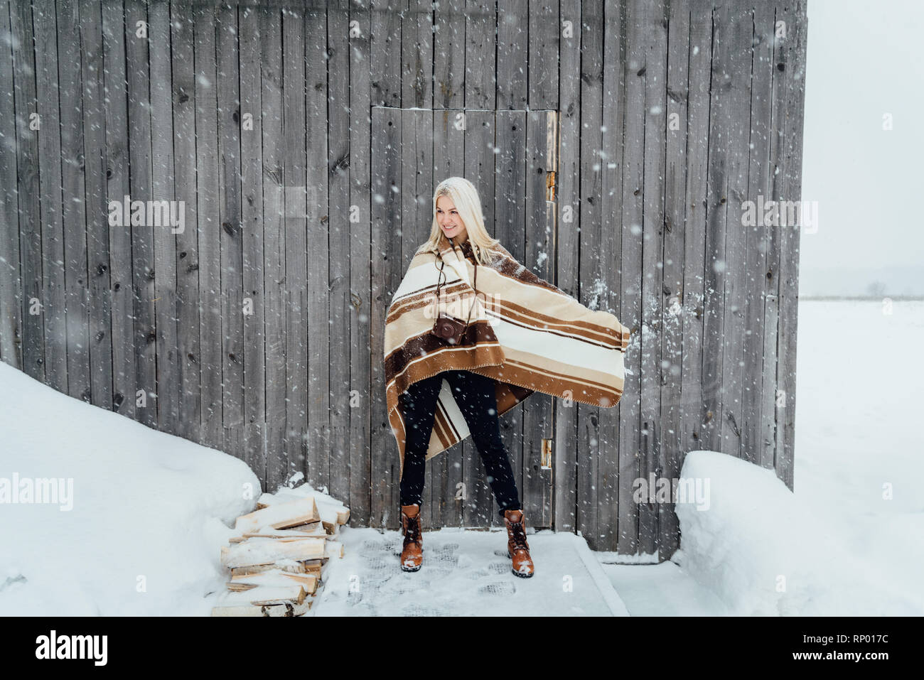 Beautiful blonde girl with a vintage camera smiling on a wooden wall background. Nikola-Lenivets, Russia Stock Photo