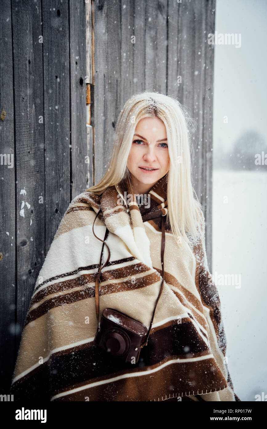 Beautiful blonde girl with a vintage camera smiling on a wooden wall background. Nikola-Lenivets, Russia Stock Photo