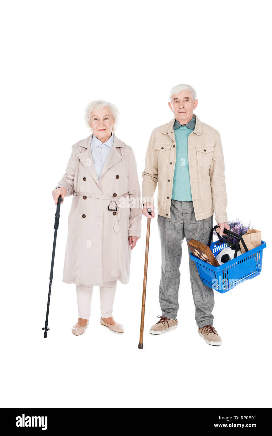 cheerful retired couple holding shopping baskets and walking canes while standing isolated on white Stock Photo