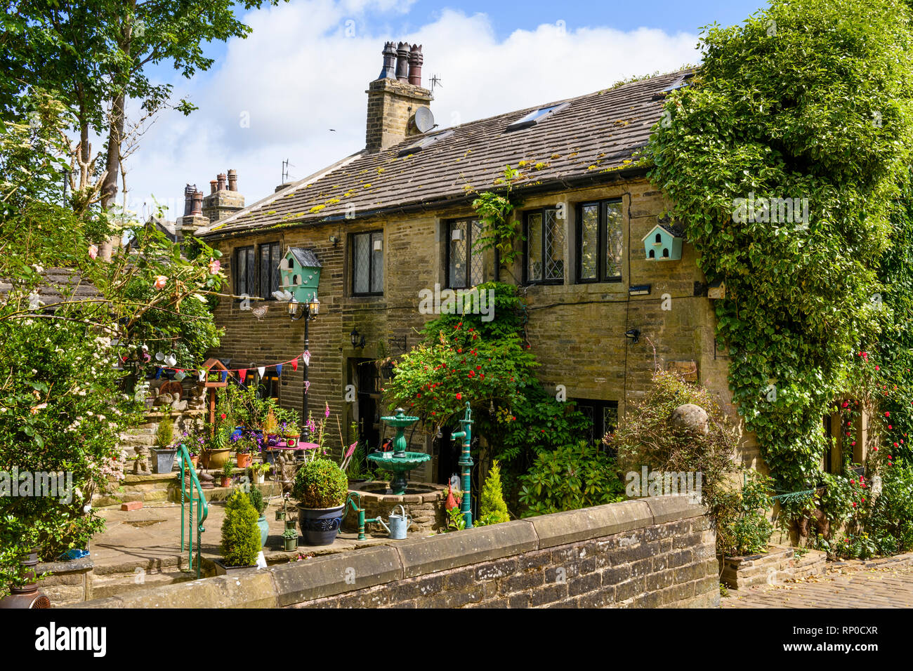 Attractive quaint traditional stone cottage with ornamental features in  patio garden (fountain & planters) - Haworth, West Yorkshire, England, UK Stock Photo