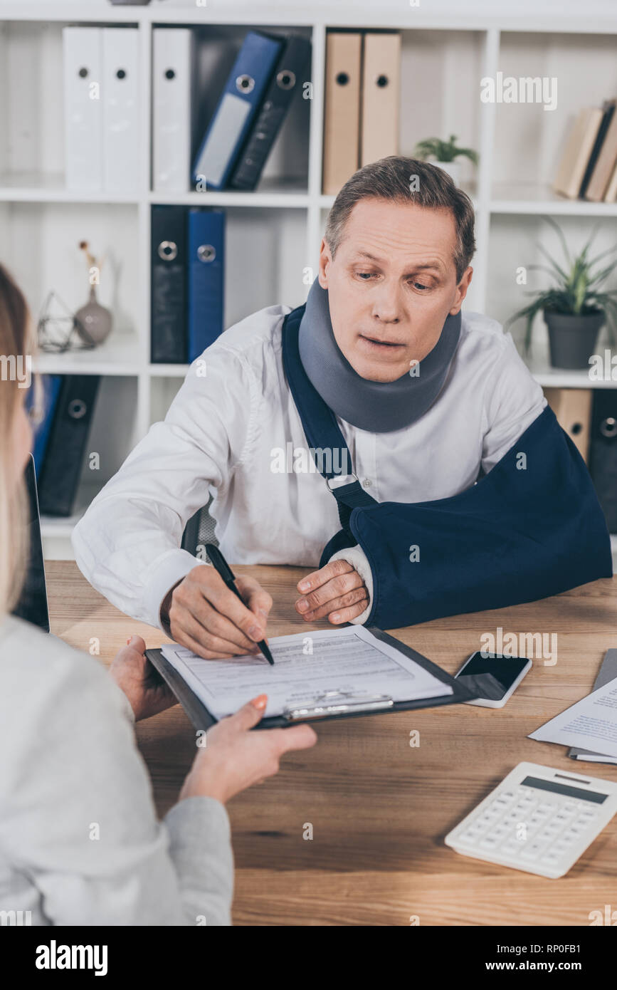 worker in neck brace and arm bandage signing while woman holding paper