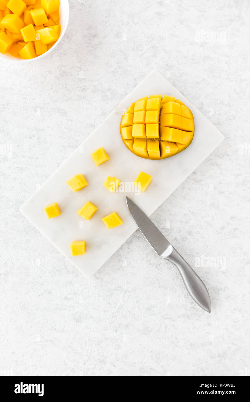 Mango cubes and cut mango half on white marble chopping board and in a white bowl. Top view. Stock Photo