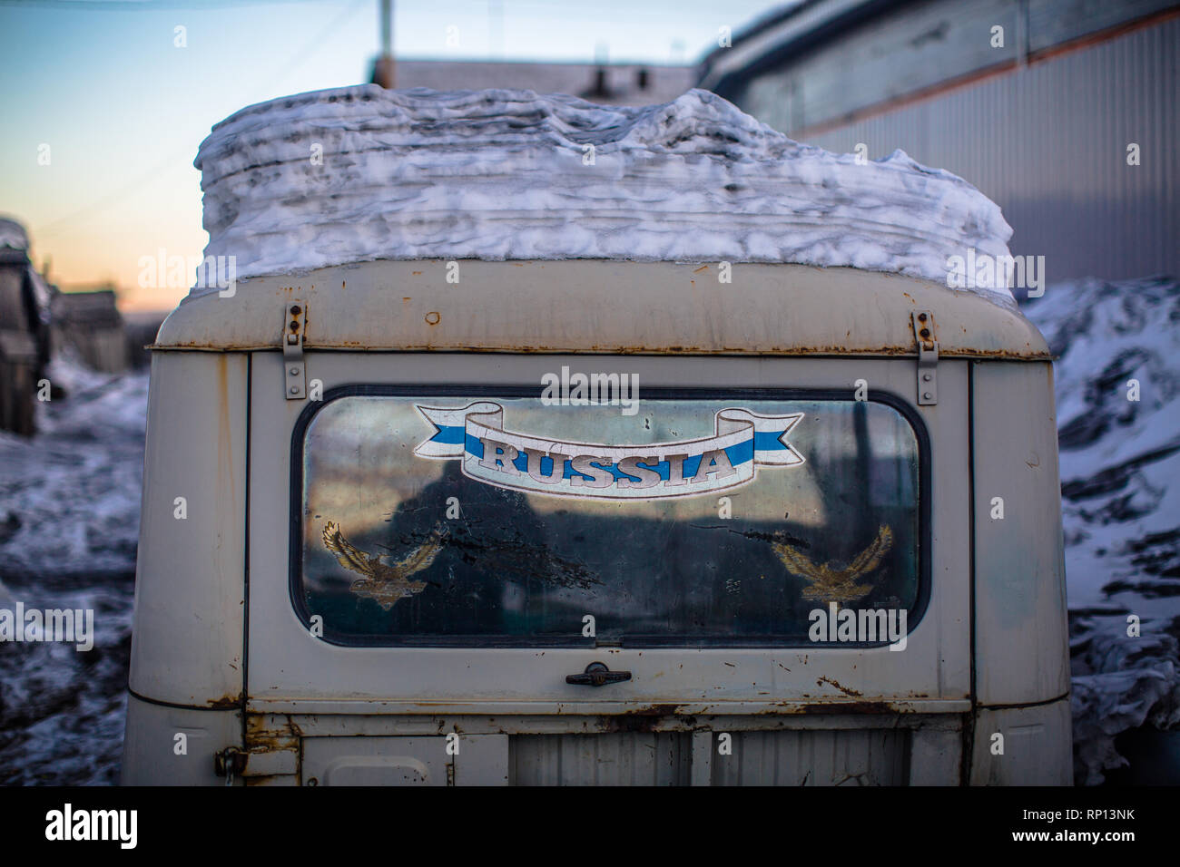 A UAZ-469 jeep parked in the background of house in Batagay,  dirty snow layers its rusty frame.  Russia Stock Photo