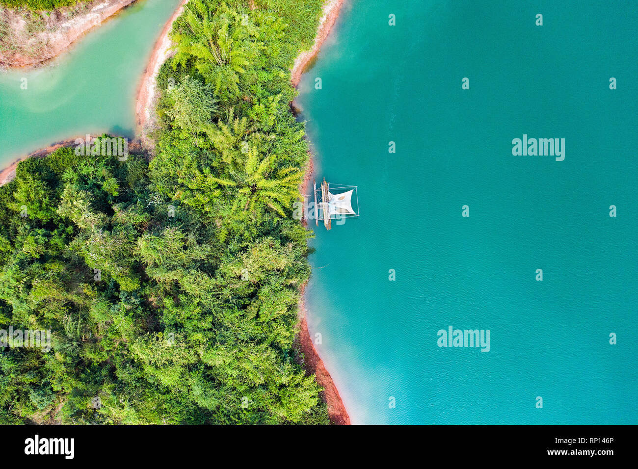 (View from above) Stunning aerial view of a a green coast of a tropical island with a traditional fishing boat in Nam Ngum Reservoir. Stock Photo