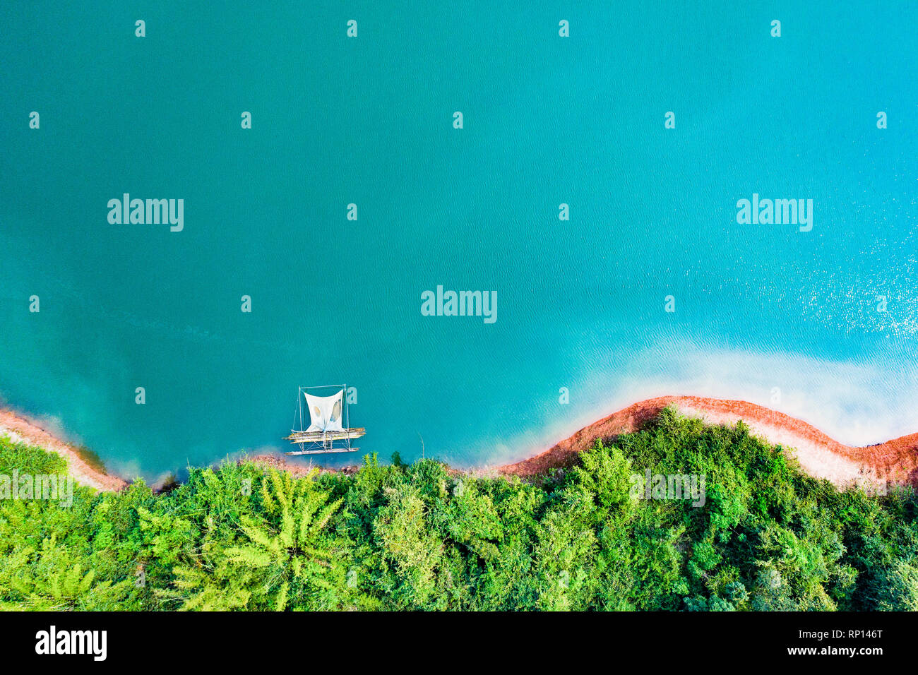 (View from above) Stunning aerial view of a a green coast of a tropical island with a traditional fishing boat in Nam Ngum Reservoir. Stock Photo