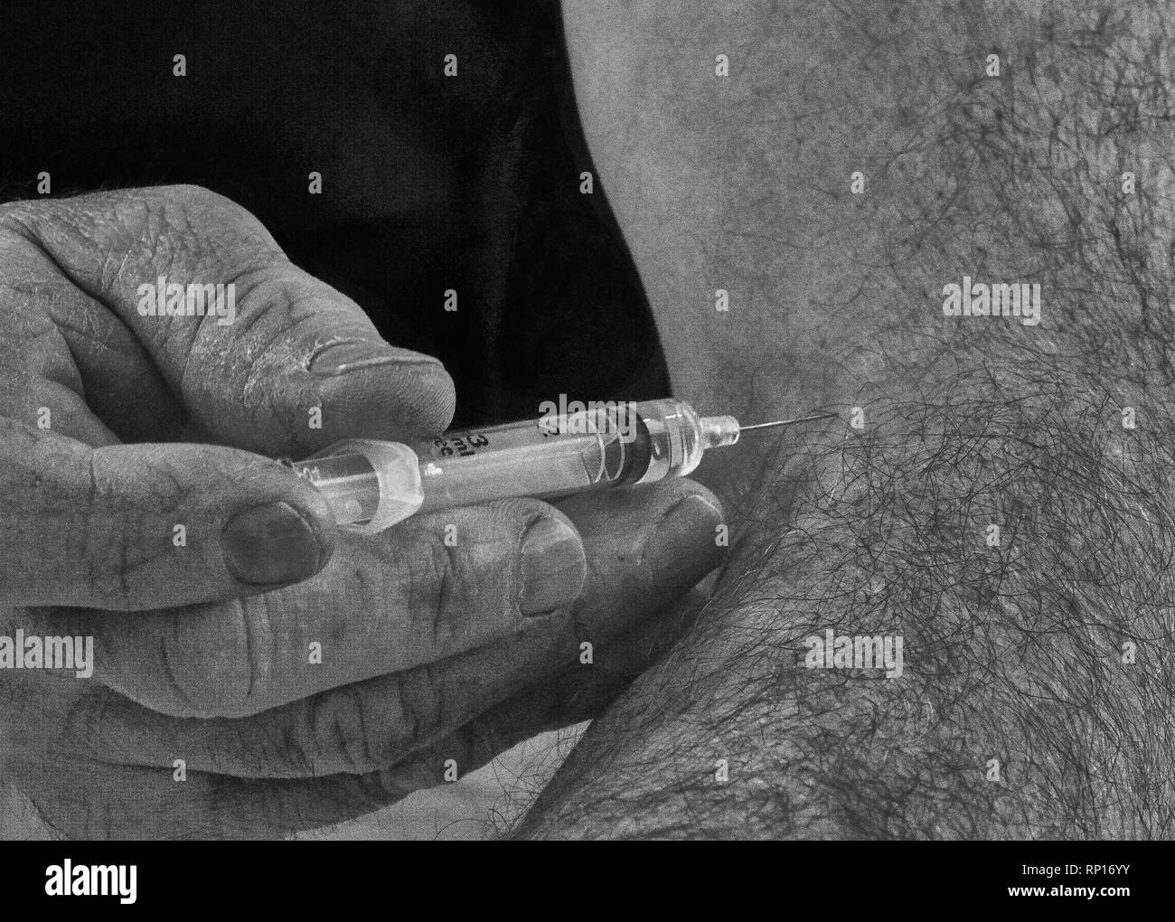 An close up image in back and white of a man holding a syringe with the needle inserted into his arm having just injected himself with its contents Stock Photo