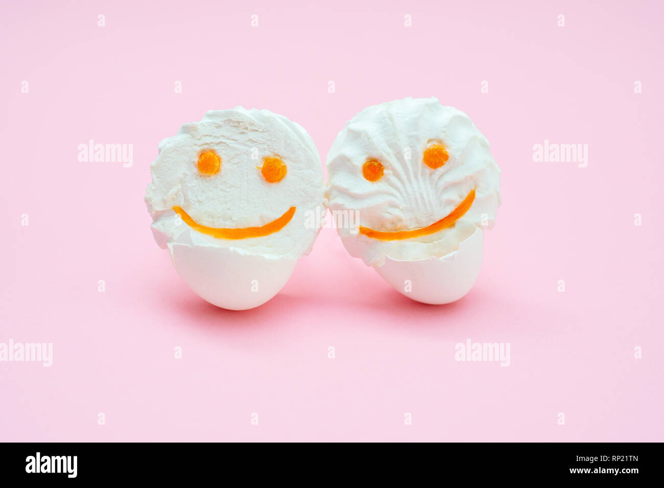 marshmallows fluff with eyes and smiles from carrots. Funny face in an egg shell stand in an embrace with each other on a pink background. isolated Stock Photo