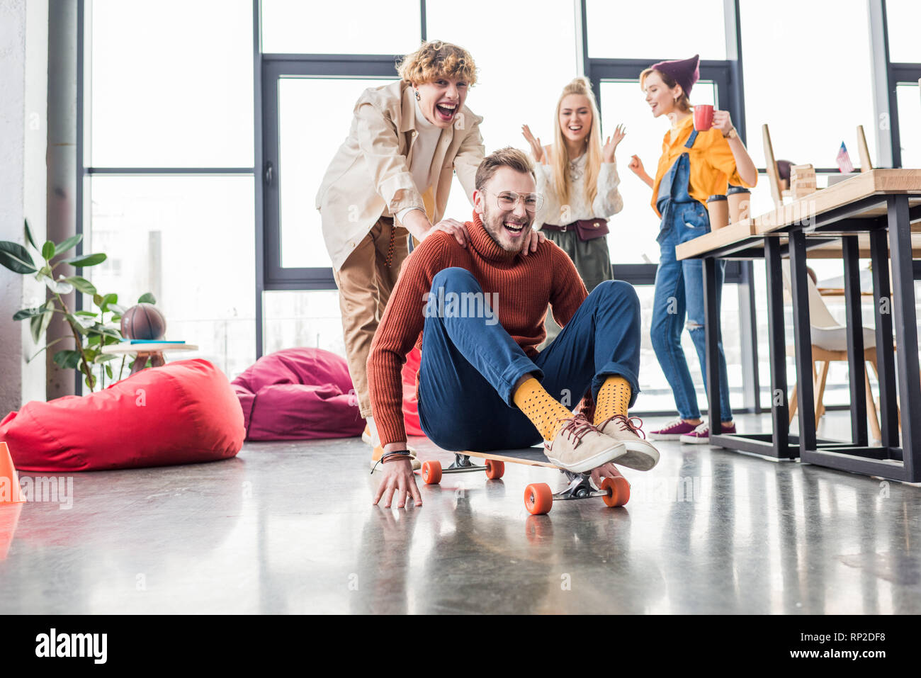 smiling casual business colleagues having fun and riding skateboard in loft  office Stock Photo - Alamy