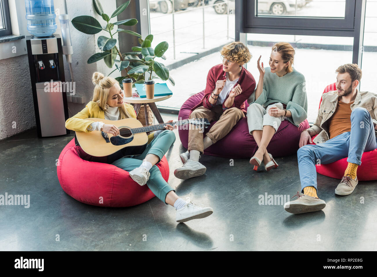 smiling group of friends sitting on bean bag chairs and playing guitar