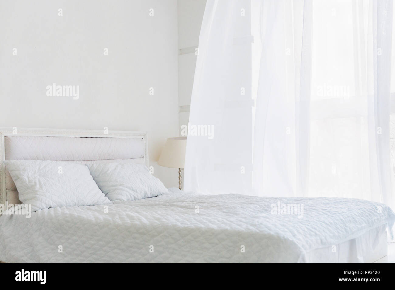 Abstract room with white bed, white walls and window with white curtain Stock Photo
