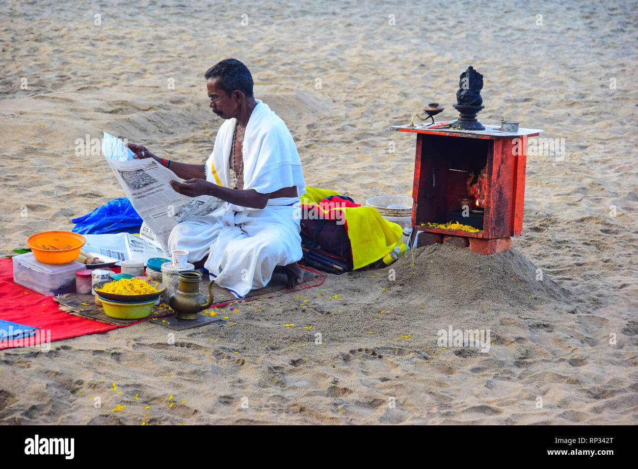 Hindu Priest reading newspaper before Hindu Ritual on Varkala Beach, Varkala, Kerala, India Stock Photo