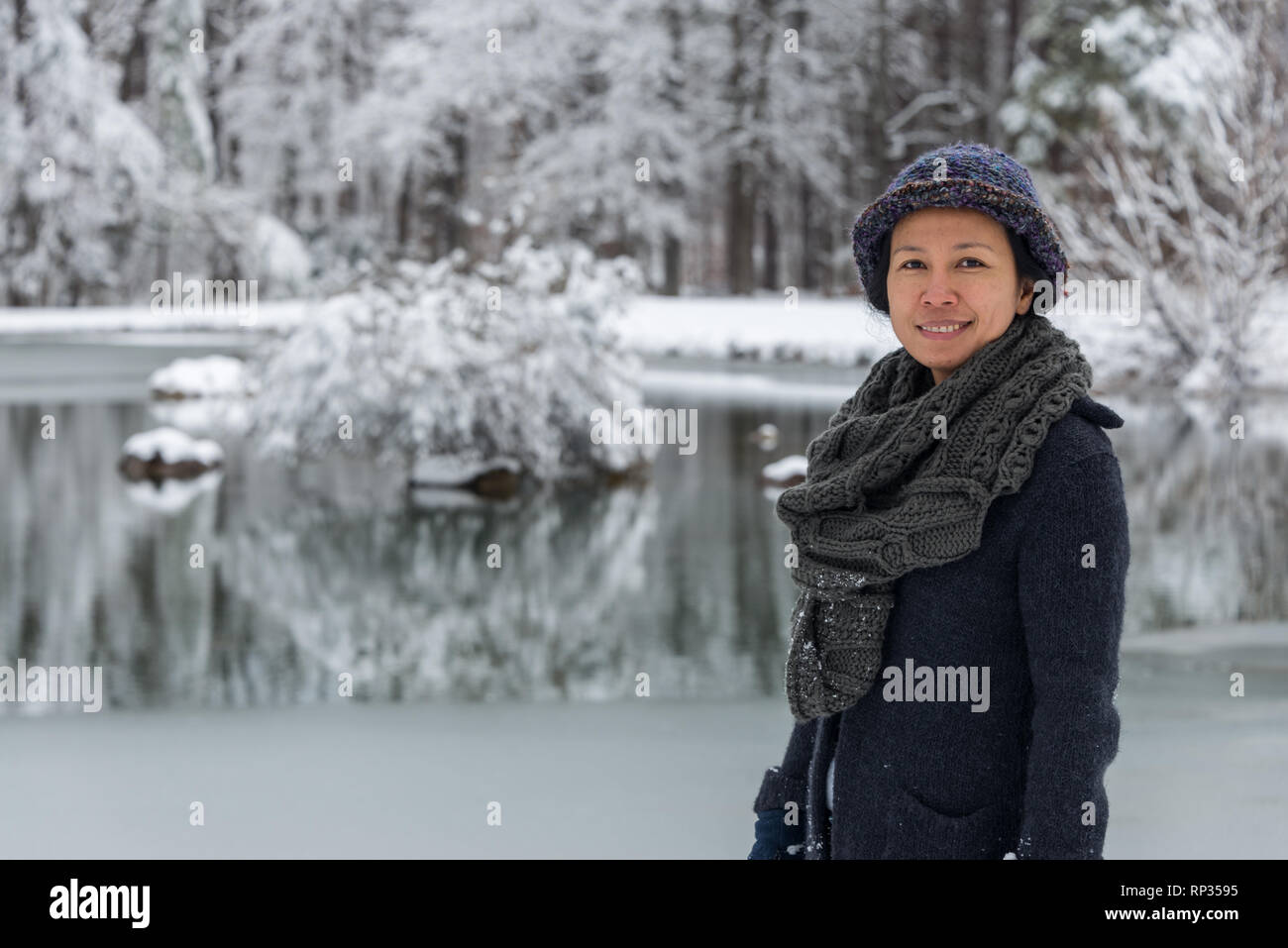 Asian woman bundled up with scarf and hat standing in front of pond Stock Photo