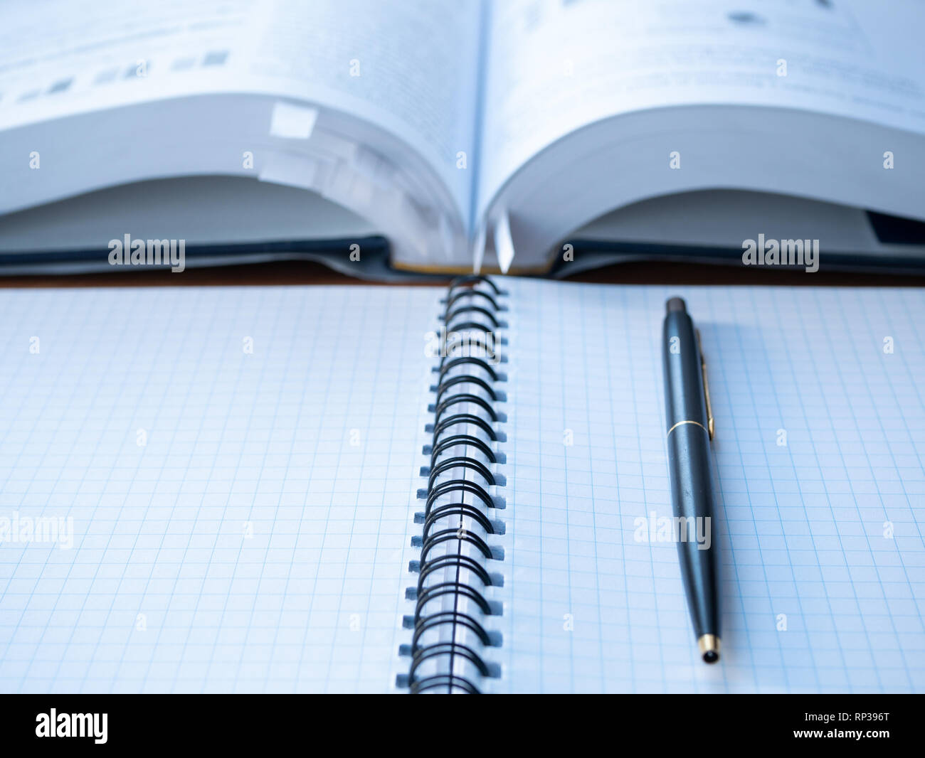 empty student notebook squared with pen and blurred book with lot of bookmarks as background. closeup image depict education process Stock Photo