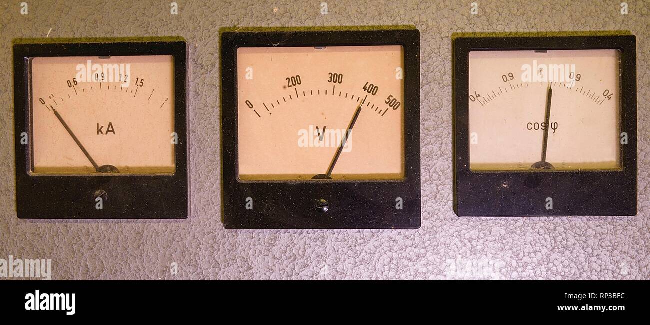 Three old analog instruments - Power factor meter, voltmeter and ampere meter isolated on grey background. Stock Photo