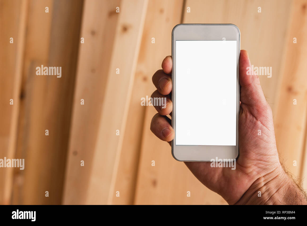 Small business woodwork entrepreneur holding modern smartphone device with blank mock up screen over workshop desk with planks Stock Photo