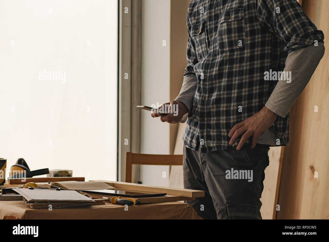 Carpenter is using smartphone for  texting in woodwork workshop Stock Photo