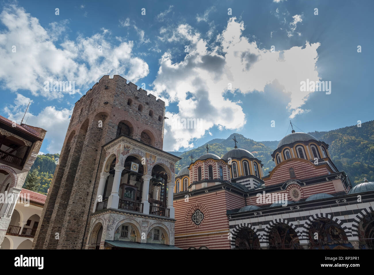 Looking up to the Tower of Hrelyu and cupola-topped main church of Rila Monastery, Bulgaria.  Sun hides behind one white cloud. Stock Photo