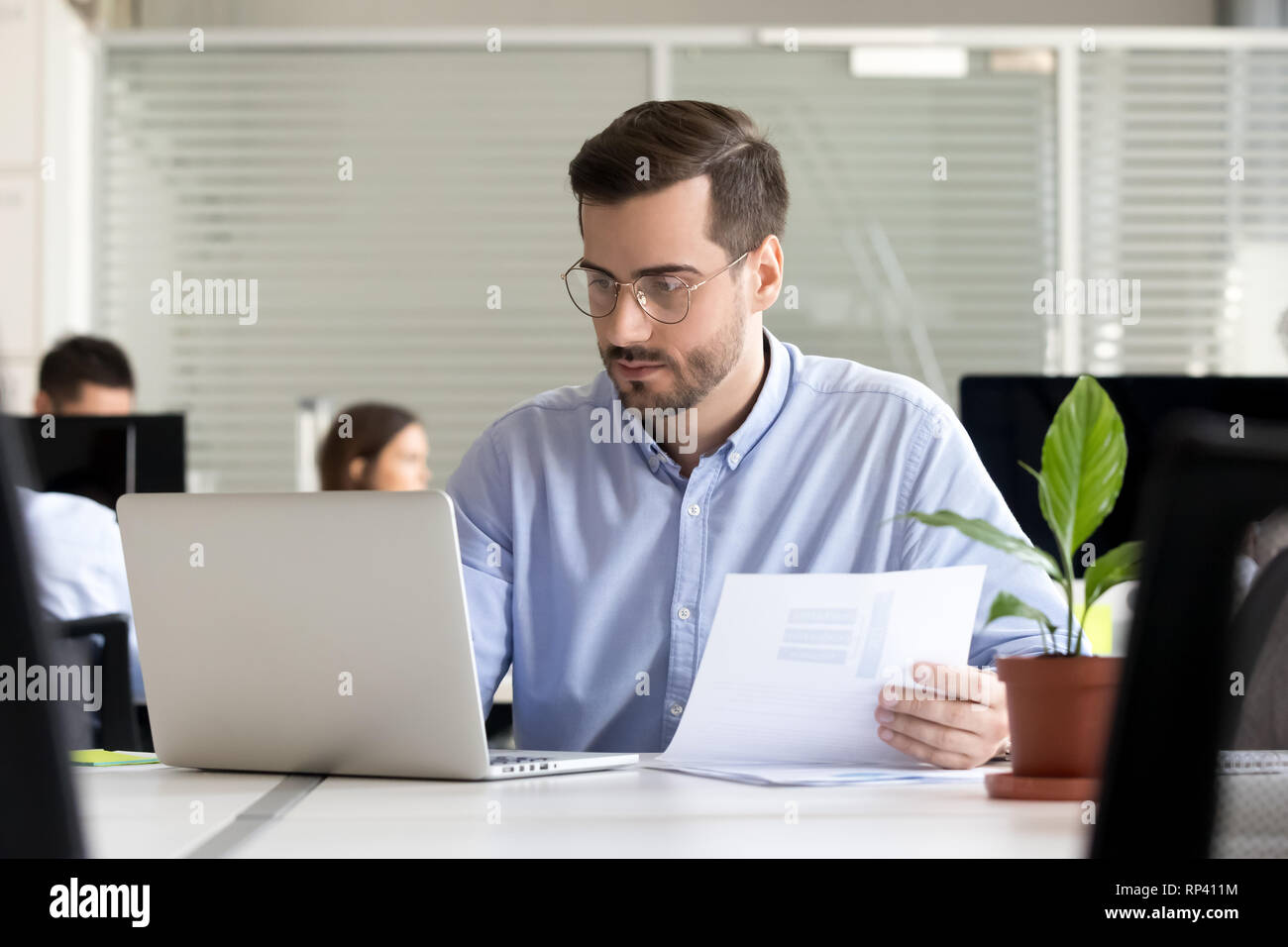 Serious thoughtful focused office worker manager sitting in coworking space office having busy day holds documentations sales statistics using compute Stock Photo