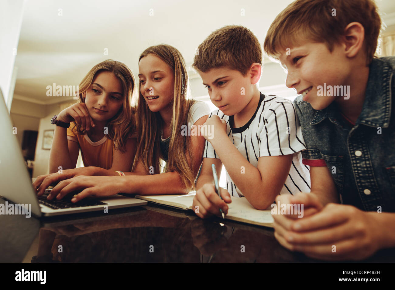 Boys and girls sitting at home studying together on a laptop computer ...