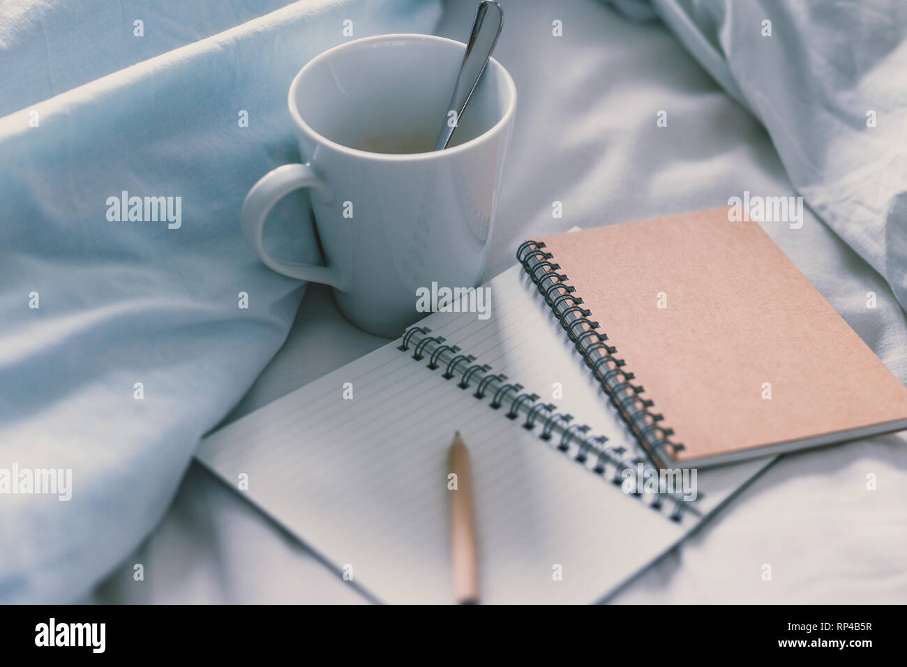 empty notepads with copyspace and pencil on bed with mug of coffee next to it, concept of starting the morning and writing a schedule or to do list Stock Photo