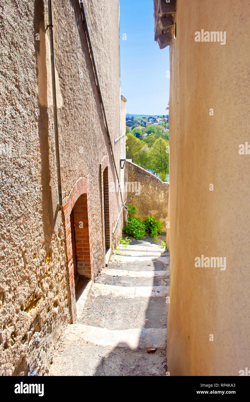 Very narrow solitary street near the city center of a small town Thouars, France. Stairs descending down and turning. Warm spring morning, vibrant blu Stock Photo