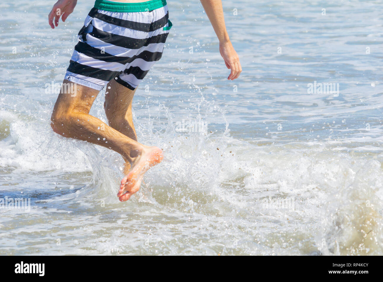 Below waist of teenager in black and white pant running in shallow ...