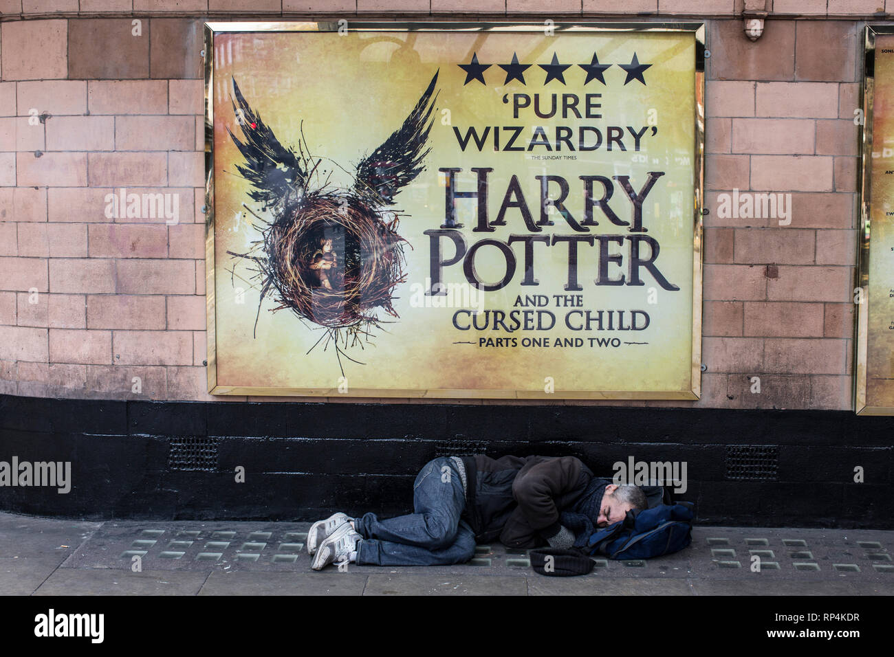 Homeless addict sleeping on the pavement underneath the sign of Harry Potter outside the Palace theatre on Cambridge Circus, London, UK Stock Photo