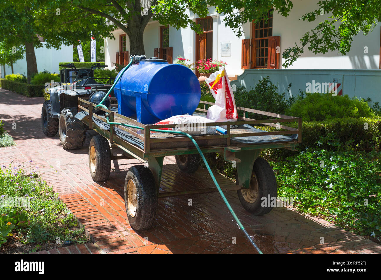 Quad bike and trailer carrying a water container and pump connected to a hosepipe which is stationary on a footpath in a garden on a hot Summers day Stock Photo