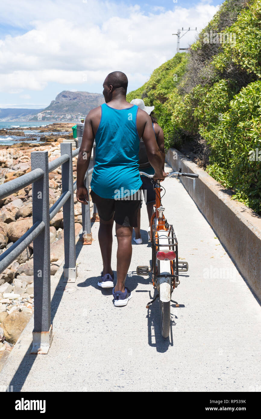 African man pushing a bicycle on a coastal footpath and walking in the ...
