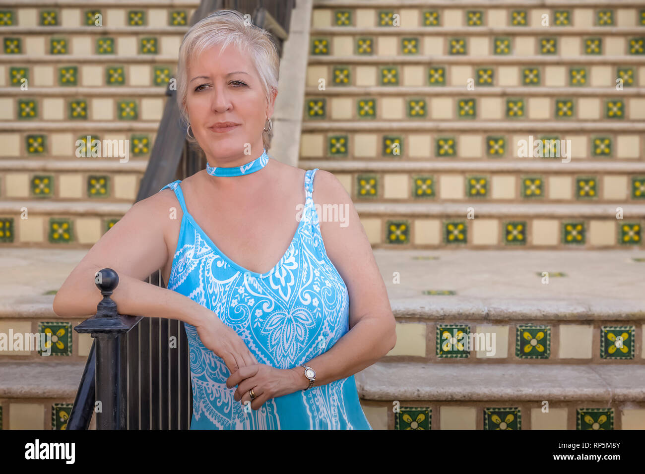 A mature modern blond woman waits at the bottom of the steps leaning on the rail. Stock Photo