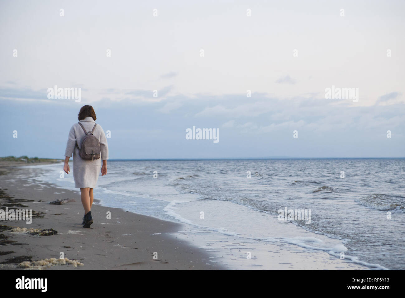 Woman in coat walking on the seashore. Stock Photo